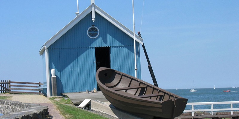Blauw reddingshuisje met houten sloep aan het water